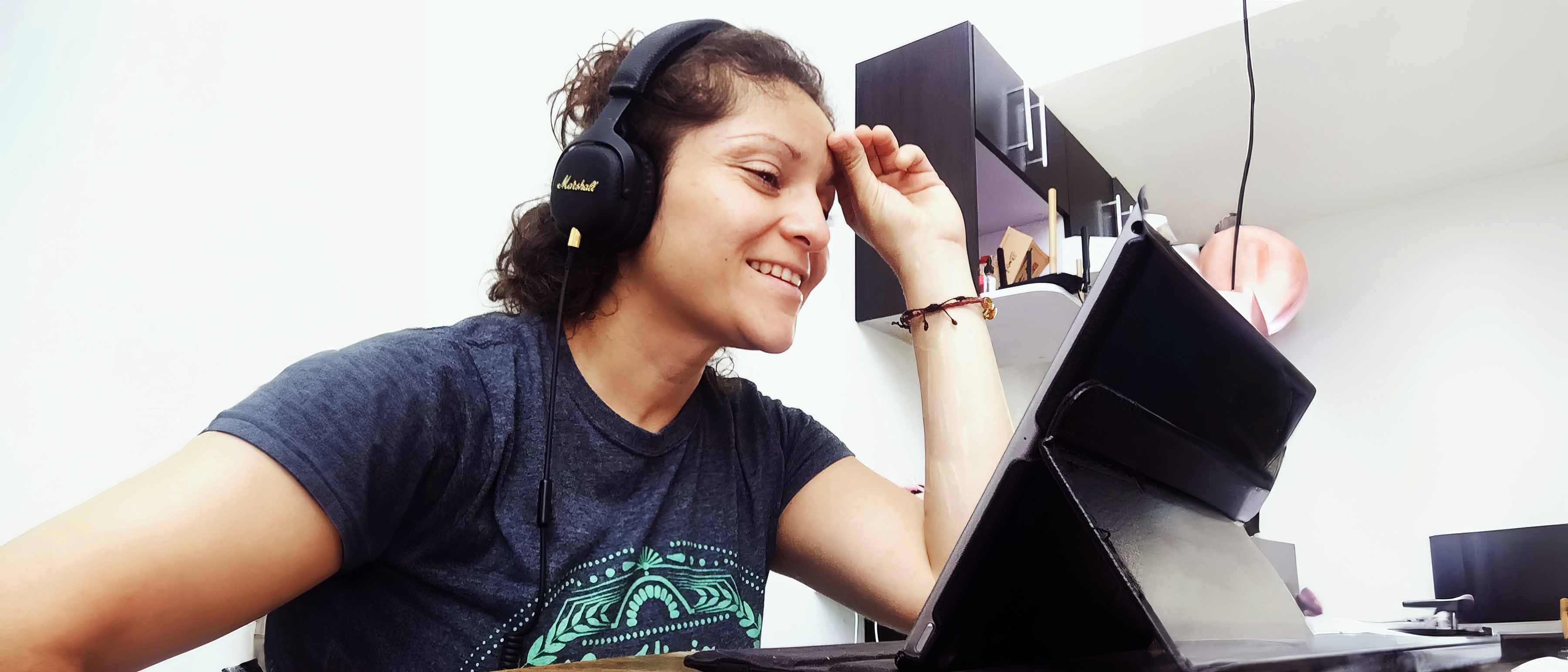 Maria Moctezuma con audífonos sonriente ante tableta.